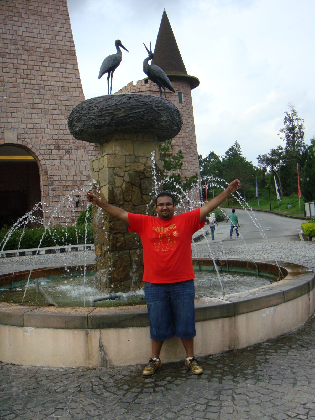 An Indian Obese Man Stand Posing In Front Of A Fountain.