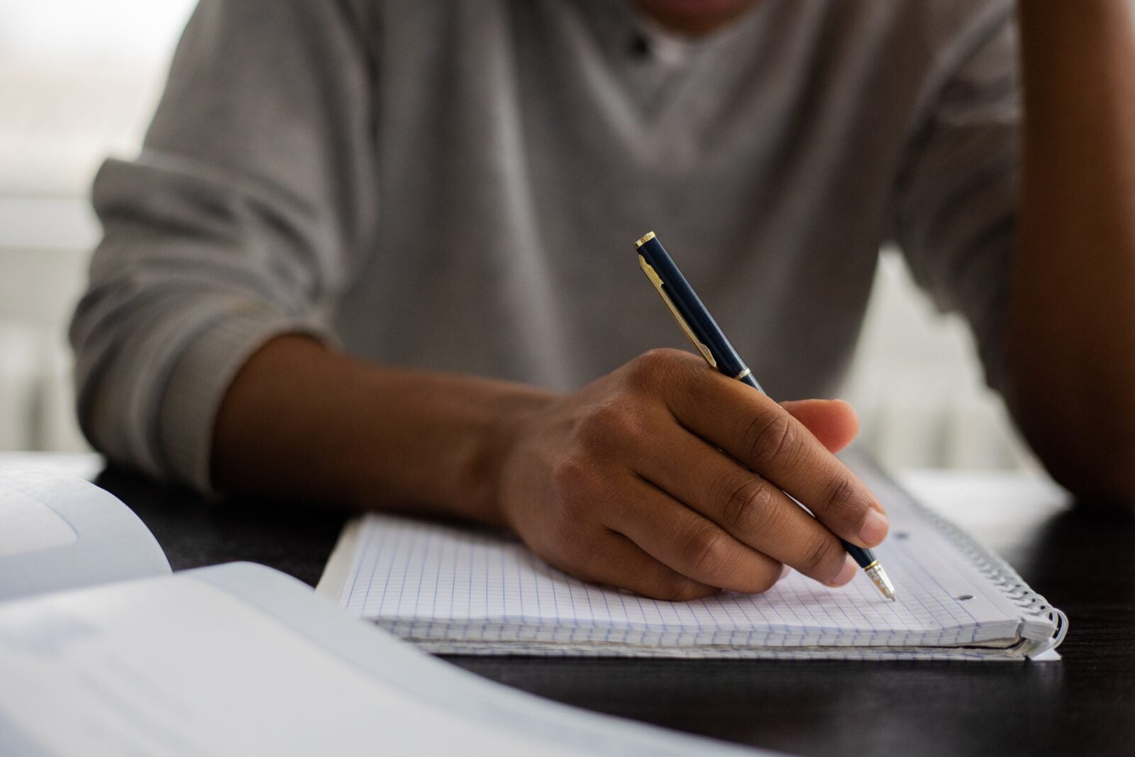 A dark skinned man holding a pen and writing on a notebook.