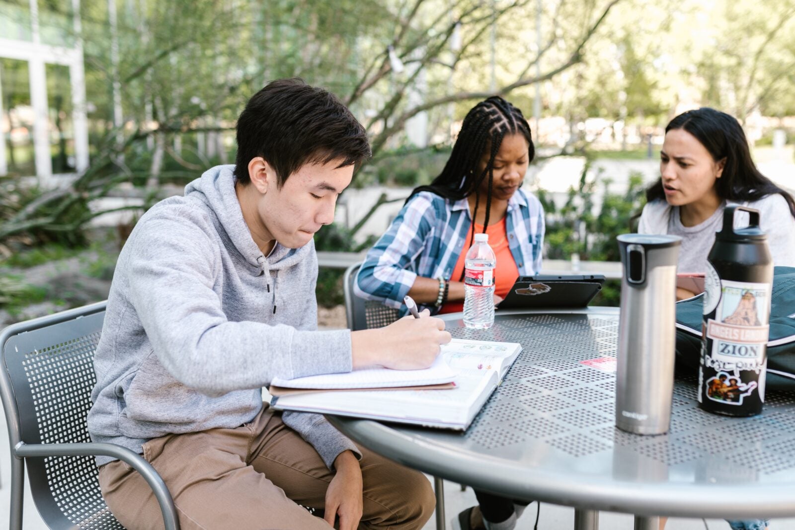 Two women and one man sitting together  at a table outdoors to study.