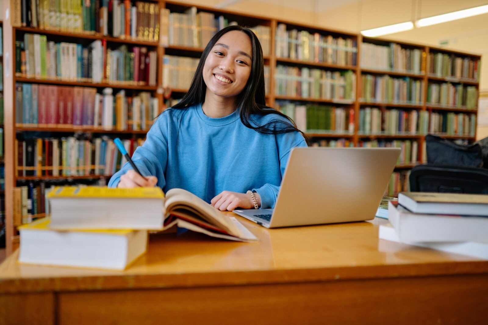 Young woman in blue sweater doing work in a library and posing while smiling