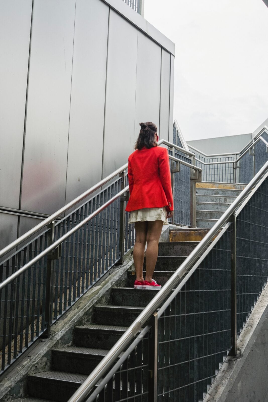 Woman in red blazer, white skirt and red shoes standing still on a flight of staircase.