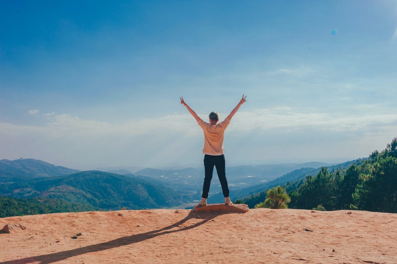 Person standing at the edge of a cliff with their arms stretched out in glory.