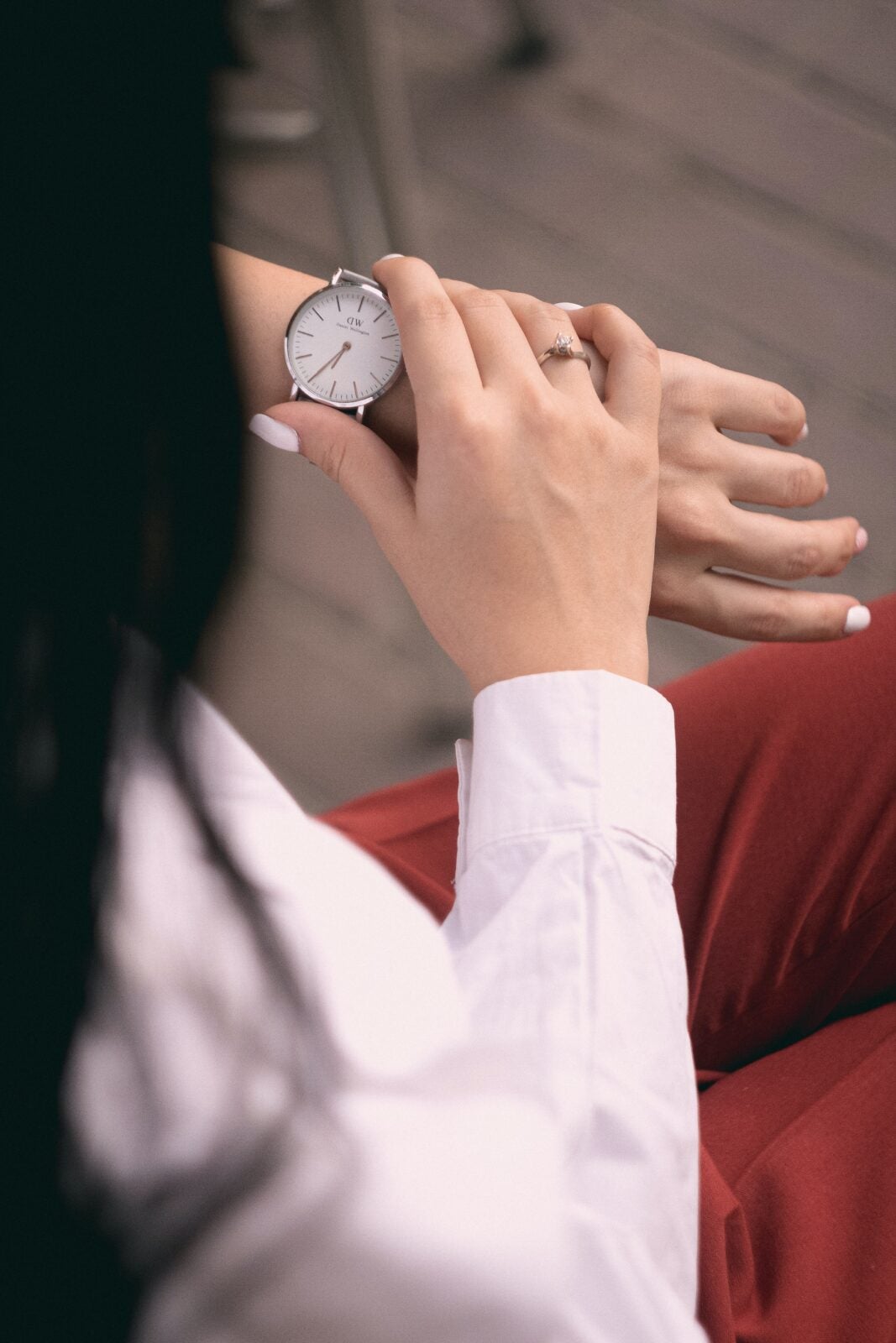 A woman with painted white nails looks at the watch on her hand.