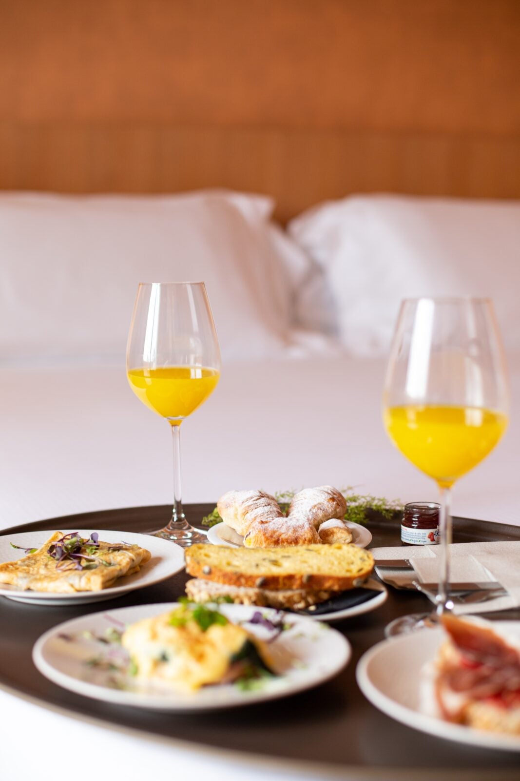 Multiple plates of breakfast foods are set on a black serving platter along with two wine glasses of orange liquid.
