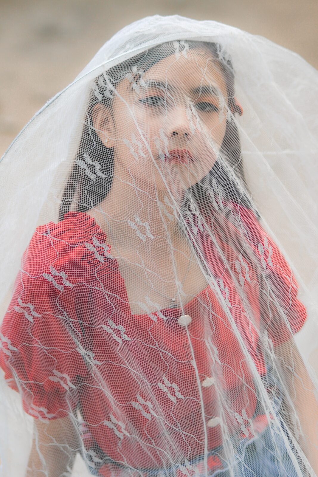 A young girl in red poses with a white veil covering her face and body.