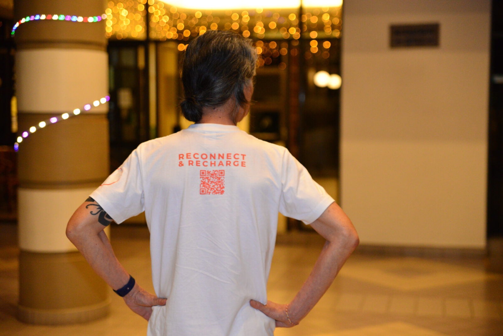 A man wearing a shirt that says reconnect and recharge faces away with his hands on his hips.