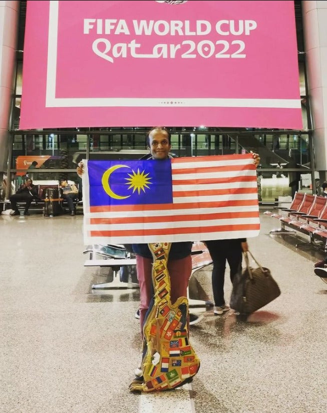 Jeshurun posing with the Jalur Gemilang in front of a banner for the FIFA World Cup in Qatar