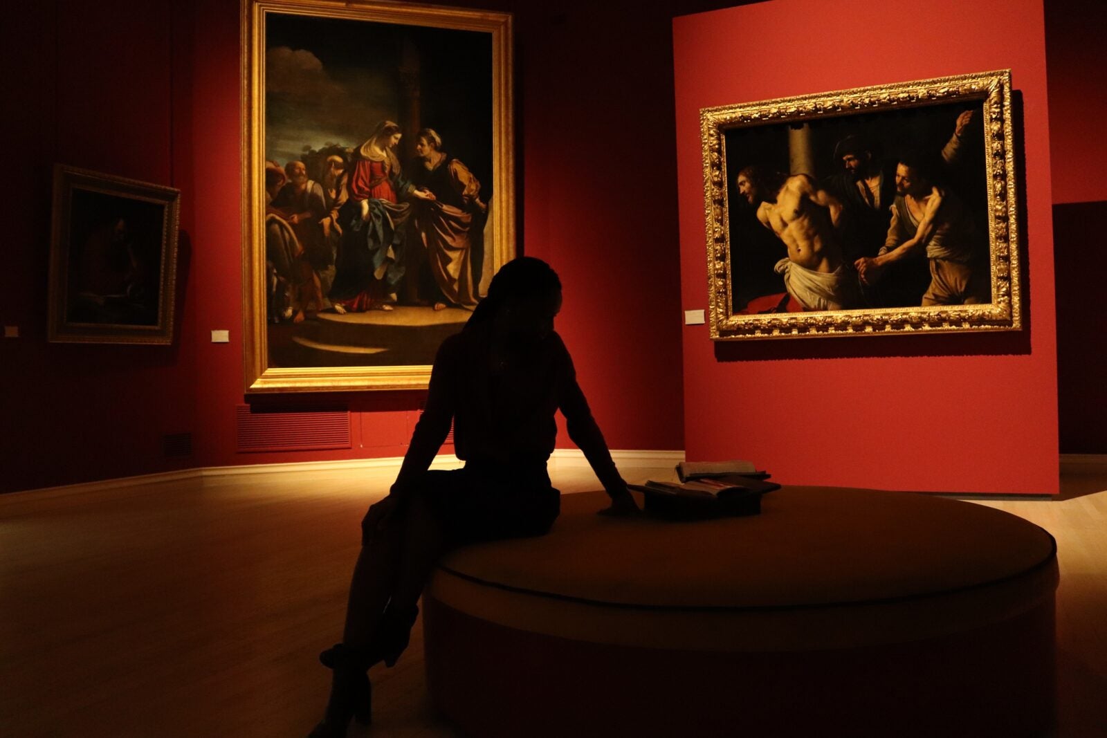 Silhouette of a woman sitting on a round chair in a museum.