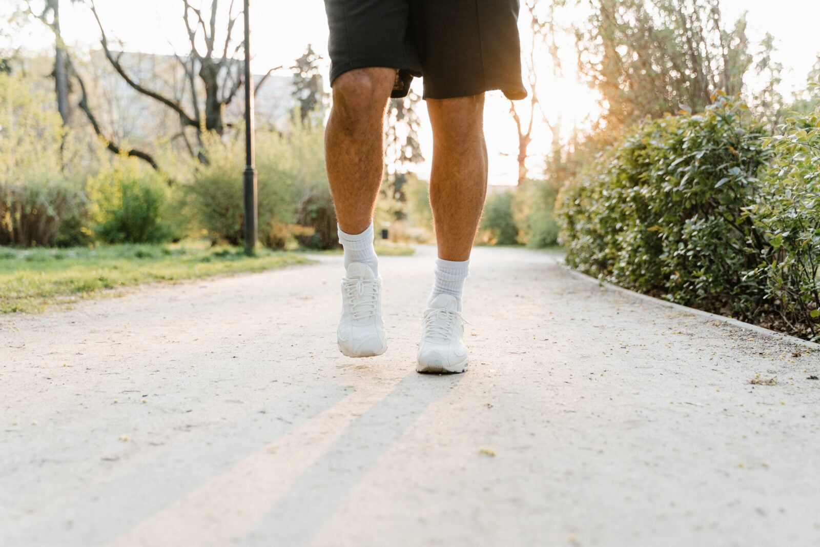 A Person Wearing Black Shorts And White Sports Shoes Walking Along A Path.