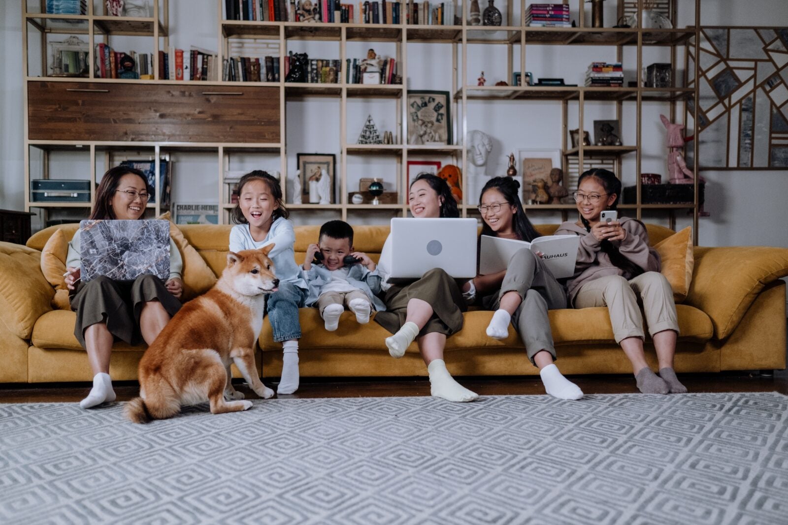 A family sits on a yellow sofa. They are laughing and enjoying each other's company while their dog sits in front of them.