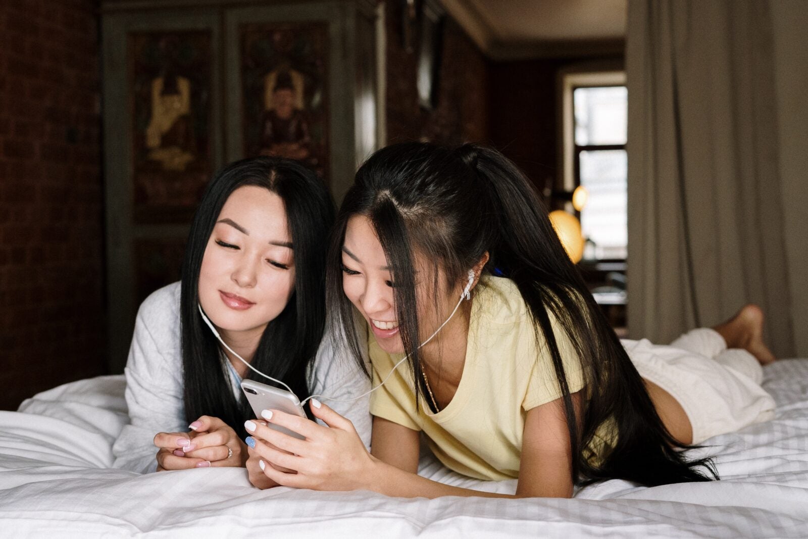 Two girls sharing an earphone and using a smartphone.