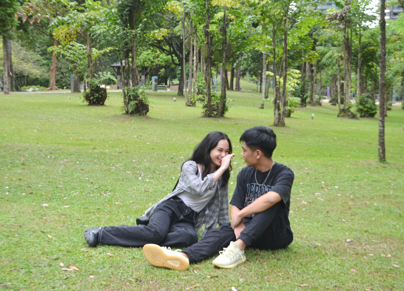A Malay Couple sitting on the grass at KLCC park, laughing as the girl reaches for the boy