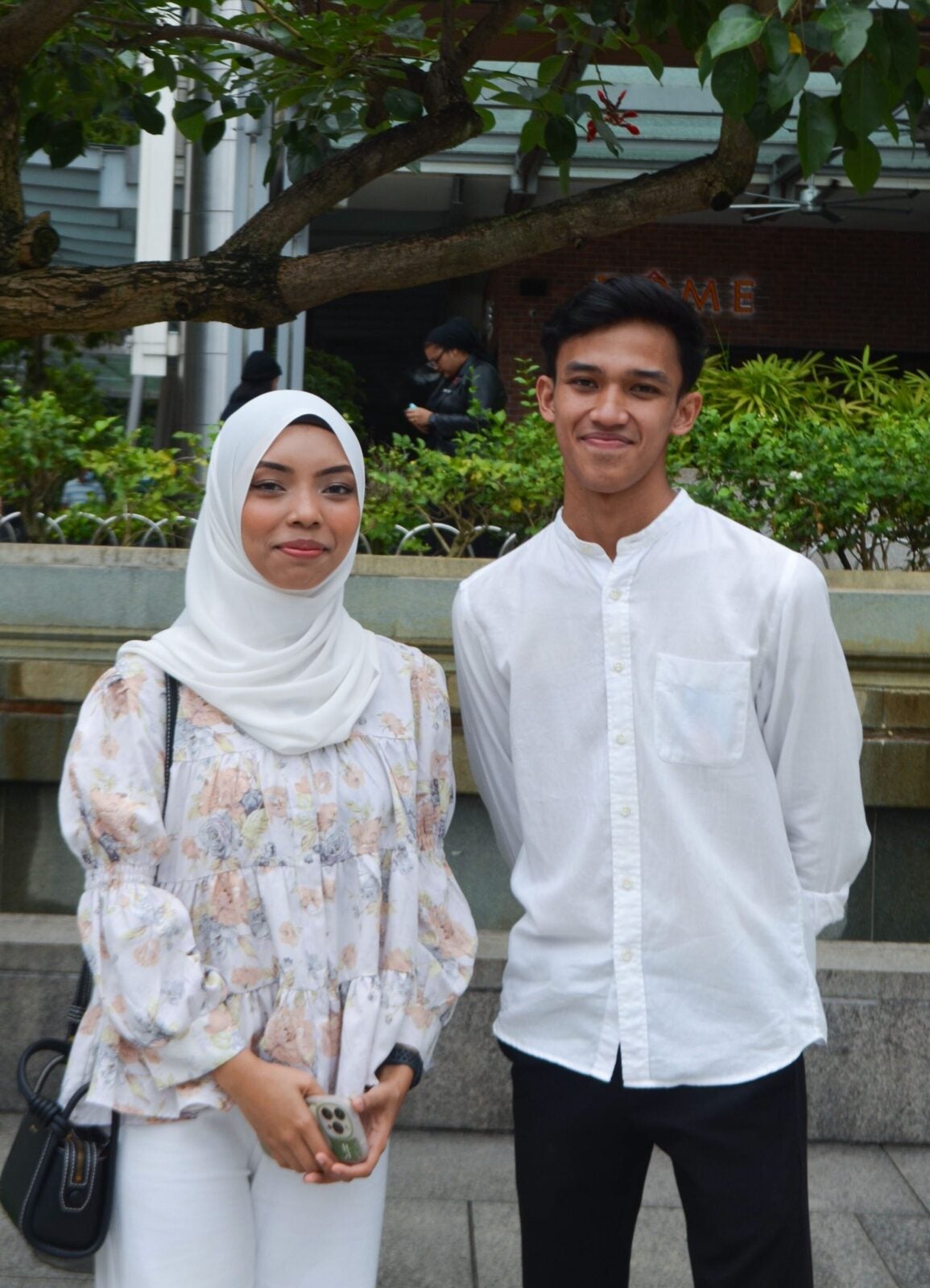 A Malay couple standing close together and smiling while standing at KLCC park