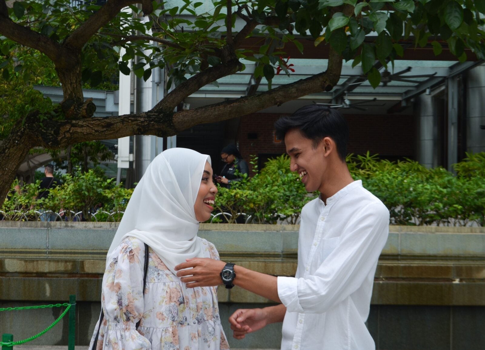 A Malay couple standing close together as the boyfriend fixes the girlfriend's hijab at KLCC park