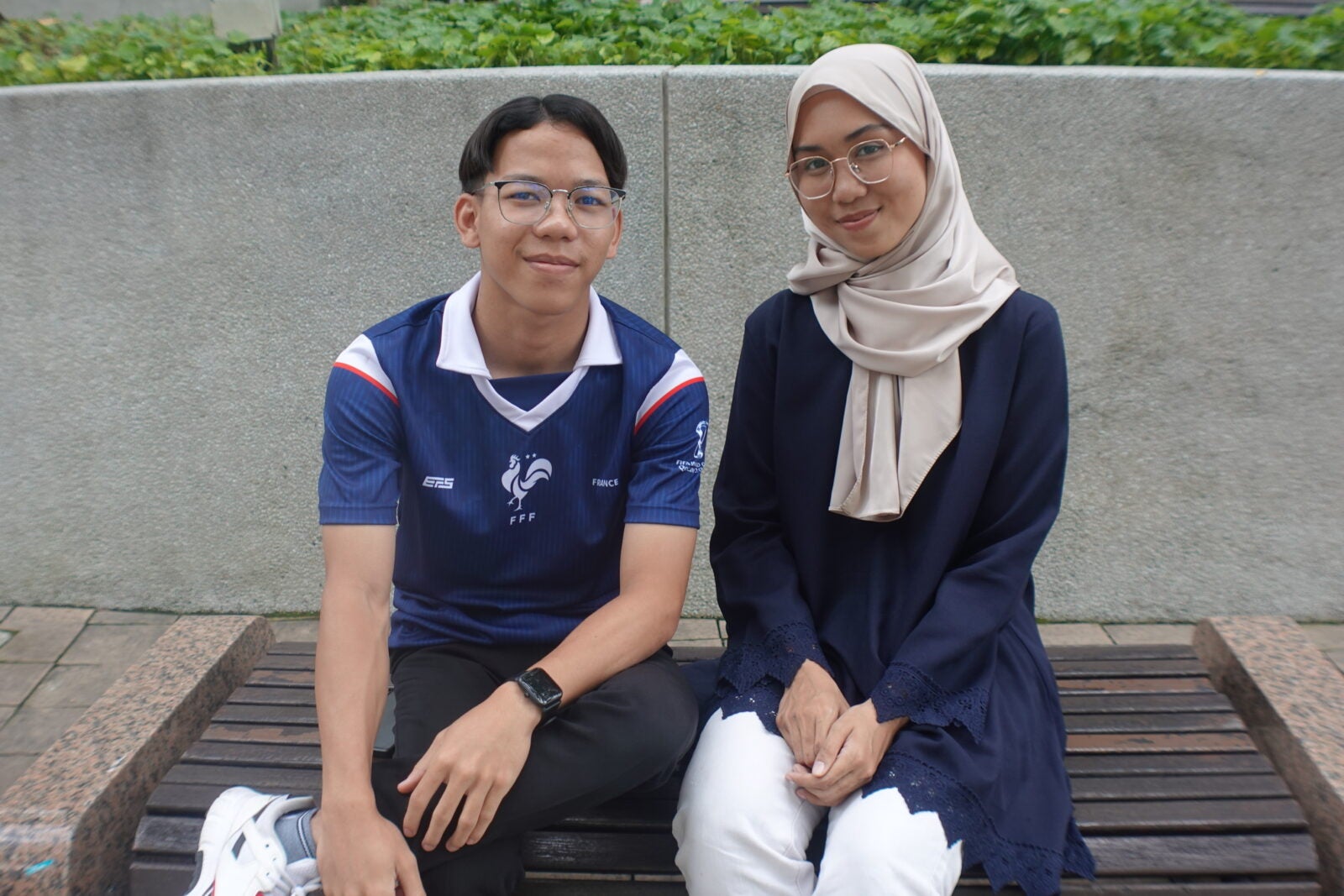 A young Malay couple sitting side by side and smiling at KLCC park.
