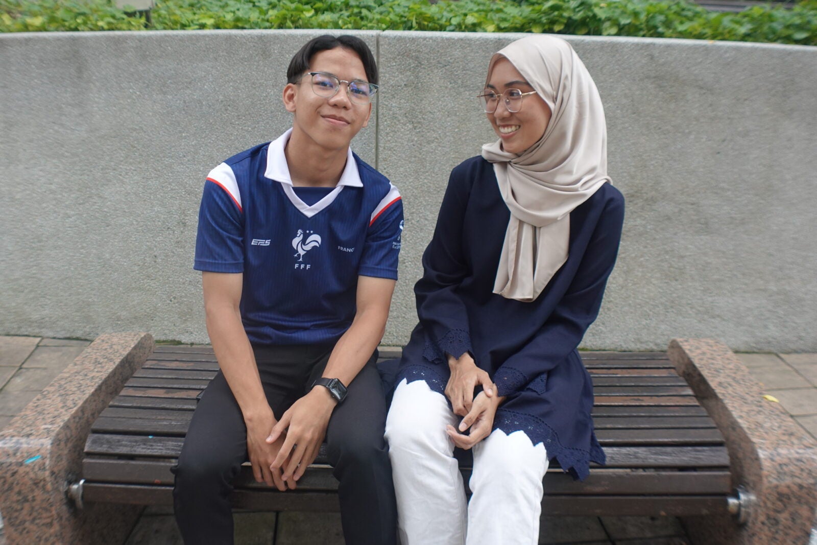A young Malay couple sitting side by side and smiling at KLCC park.