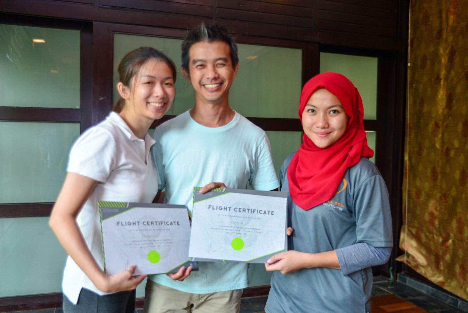 A Chinese Couple Posing With Their Flight Certificate Which Is Given By A Malay Woman In Red Hijab.