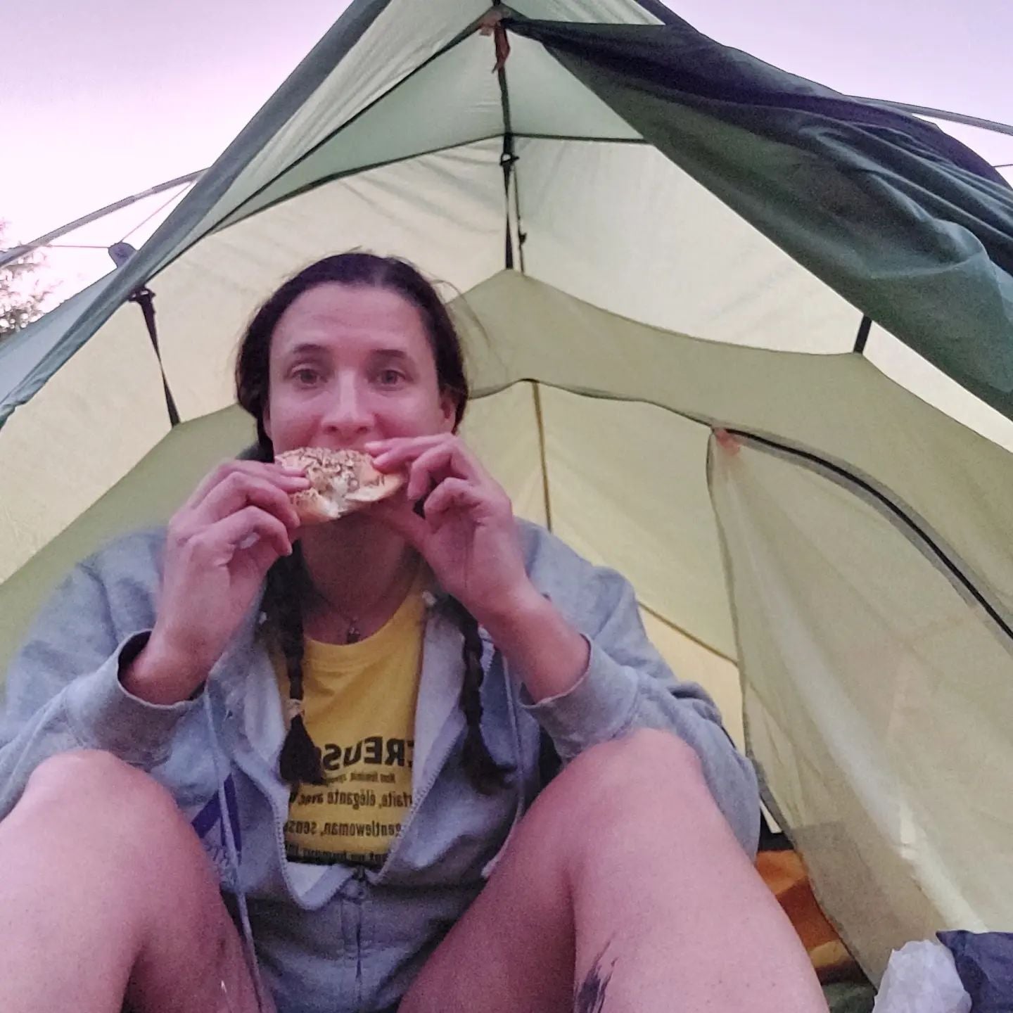 A Woman sitting at the entrance of her tent, eating bread.