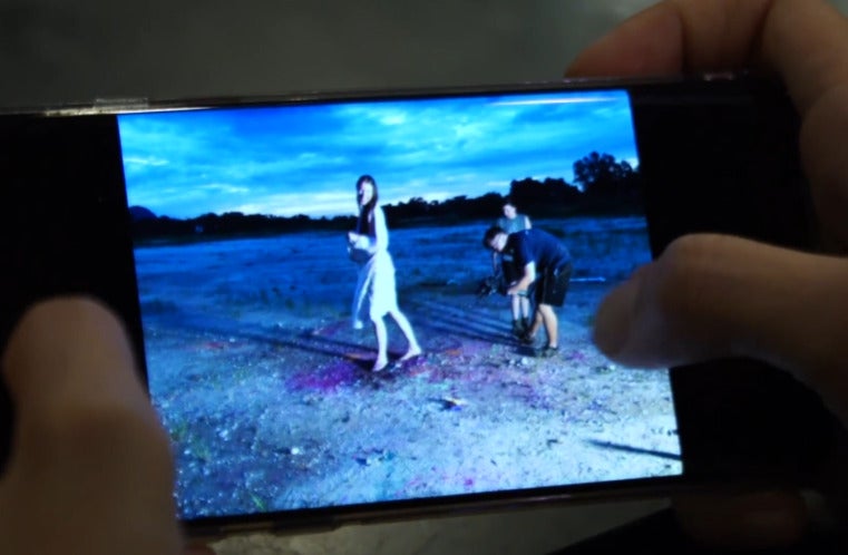 Close up of a phone screen which shows a photo of a Swiss-Malaysian woman holding a huge camera while a woman poses in front of her at a beach.