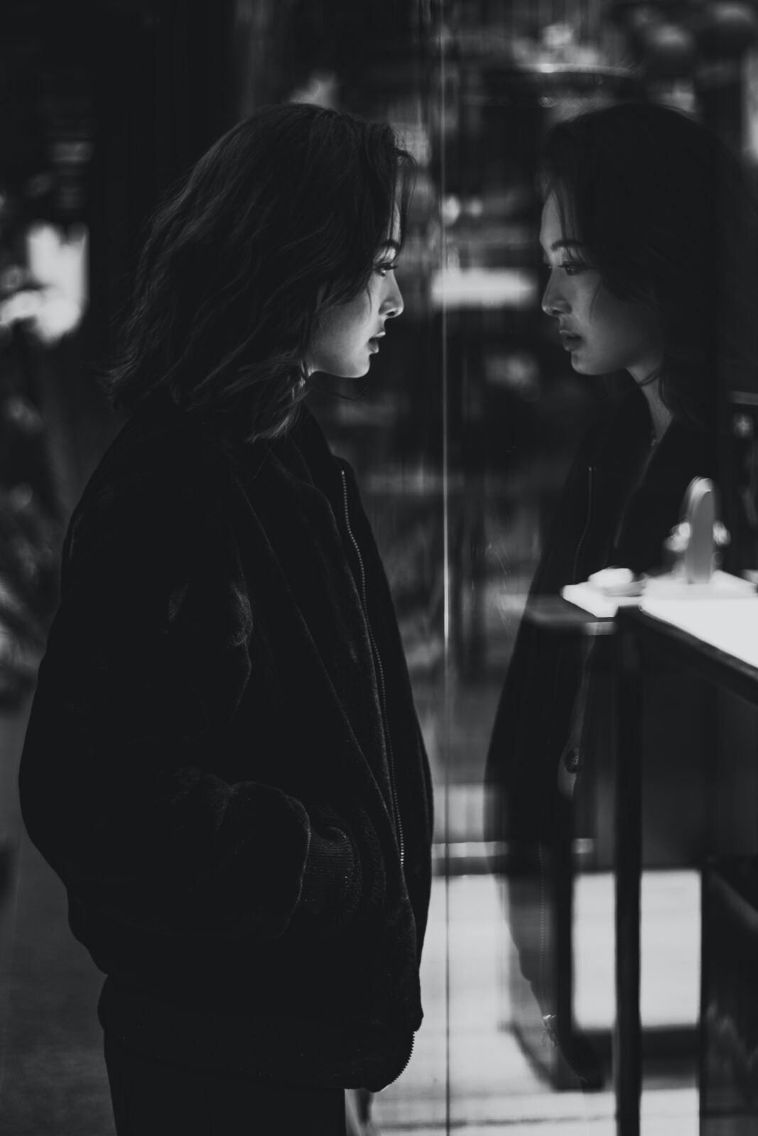 Black and White of an Asian woman wearing black jean jackets looking at her reflection.