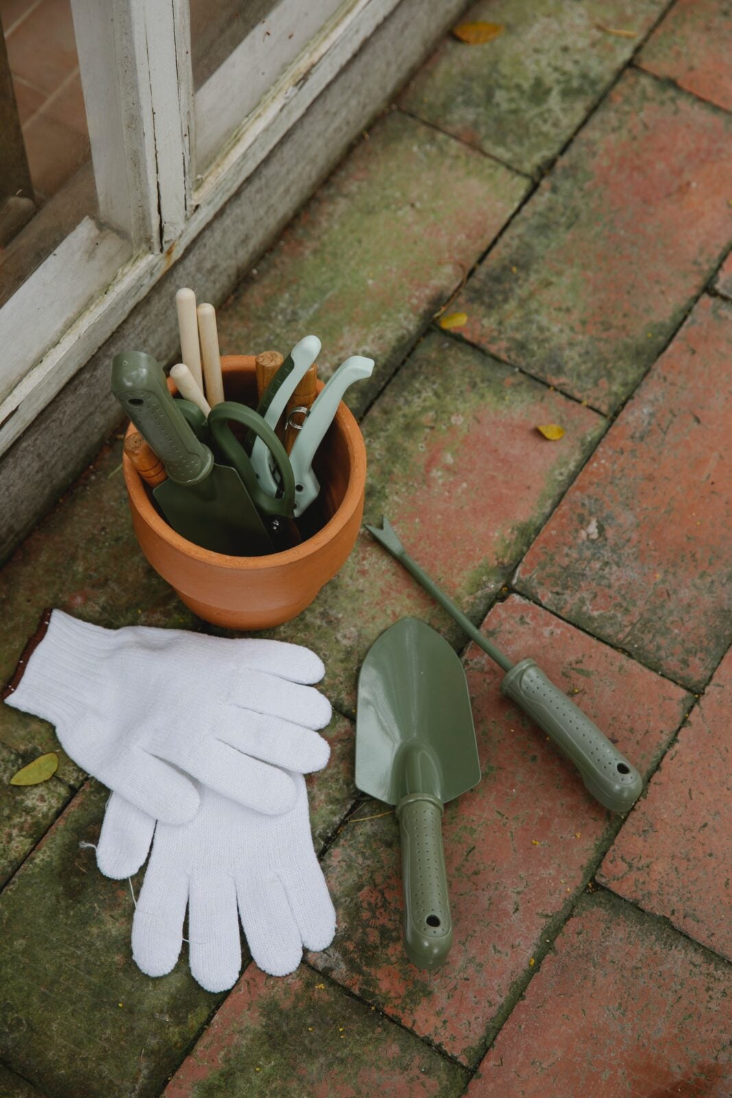 a small plant pot full of gardening tools and a white gardening glove next to it. 