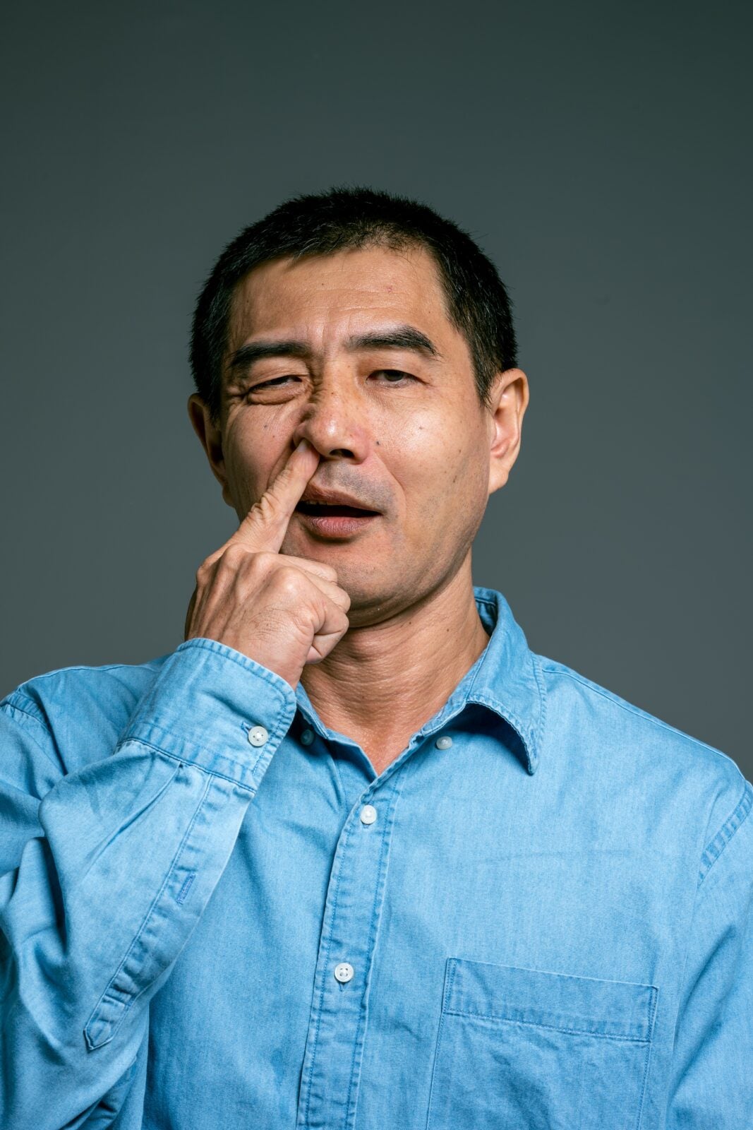 A man wearing a blue shirt digging his nose. 