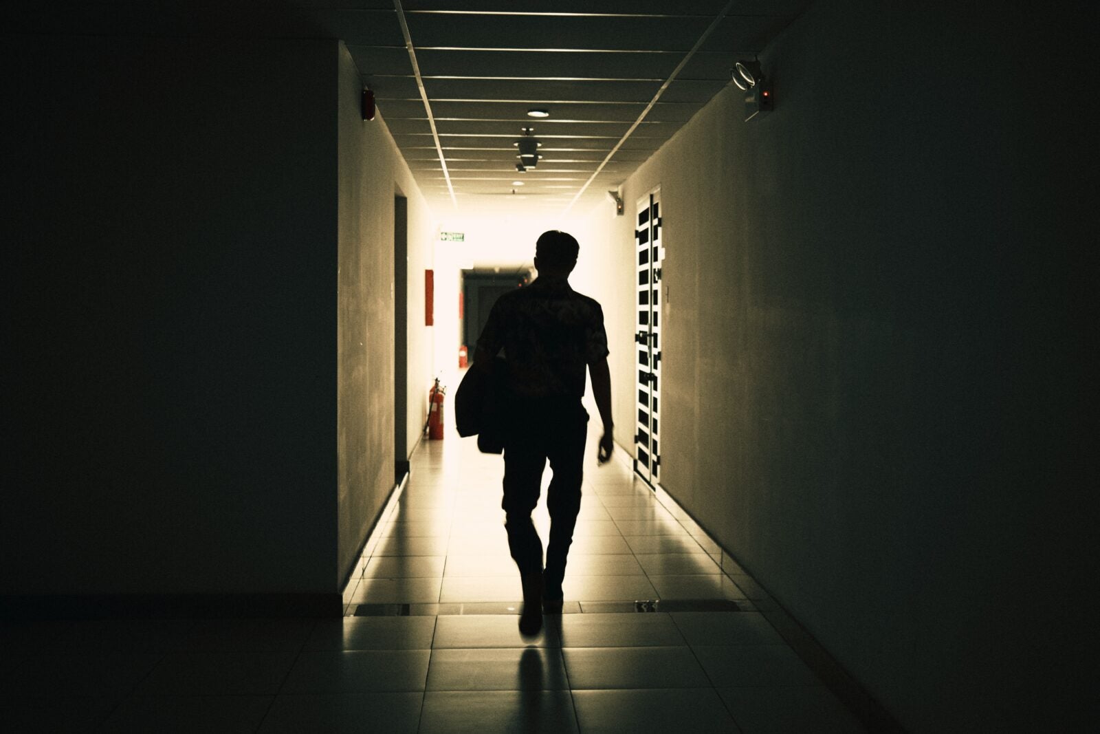 Silhouette of a man holding a bag leaving a hallway