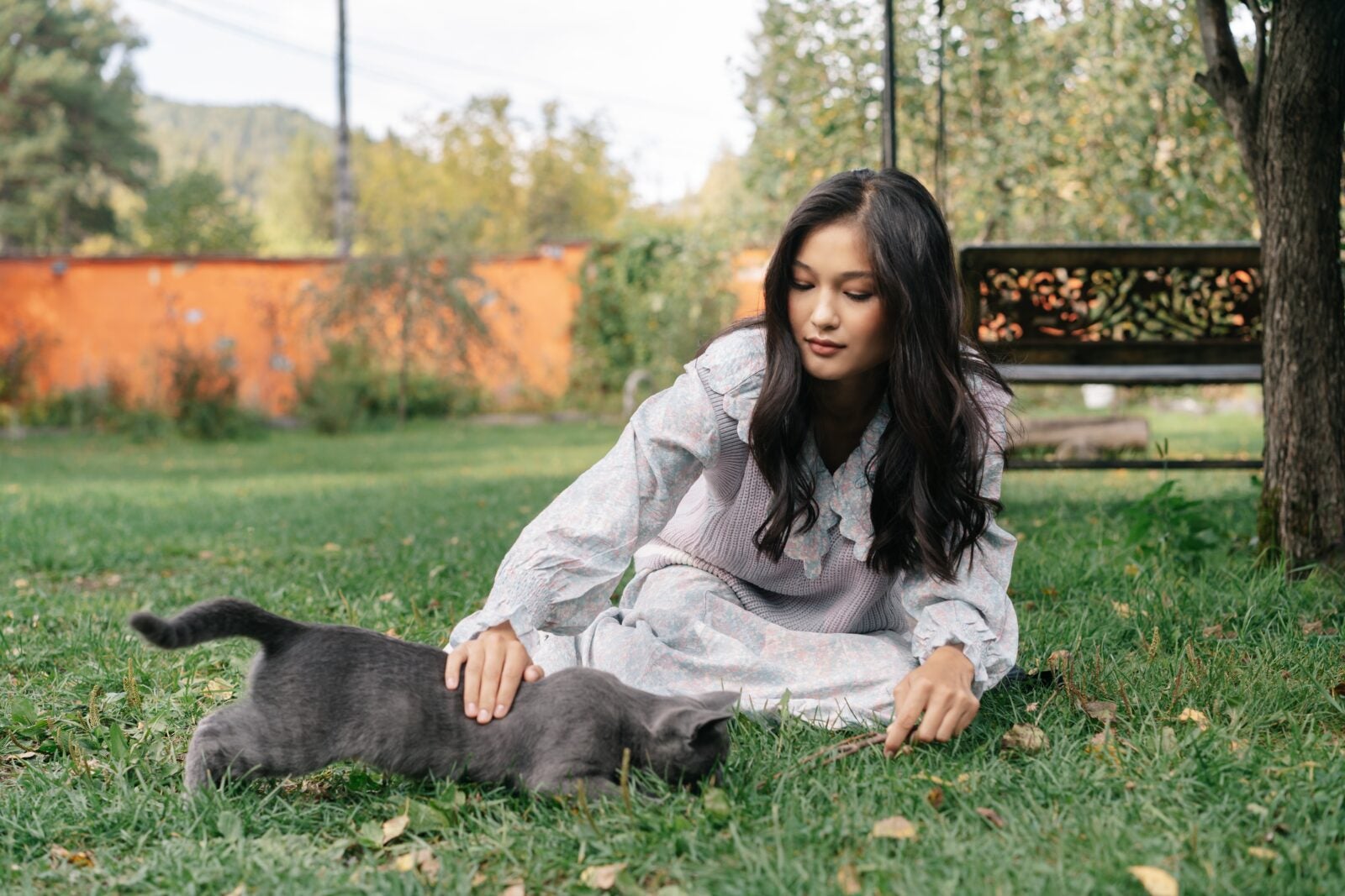 An Asian woman petting a cat while sitting on the grass.