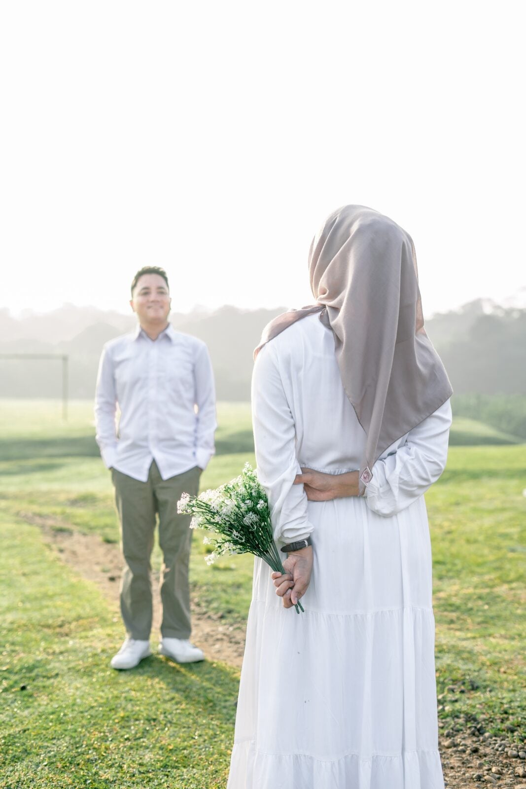 A Malay woman standing in front of a Malay Man, her hands are hidden behind her back and she is holding a bouquet of flowers.
