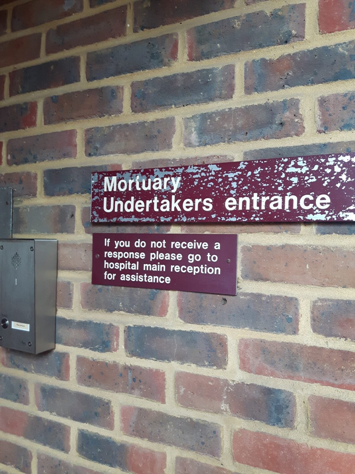 A sign on a brick wall that writes "Mortuary Undertakers entrance" at the grounds of Lewisham Hospital London, UK.