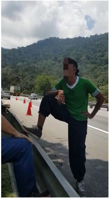 Man In Green Shirt Standing With Leg Up Against The Railing On A Highway In Malaysia, Face Blurred