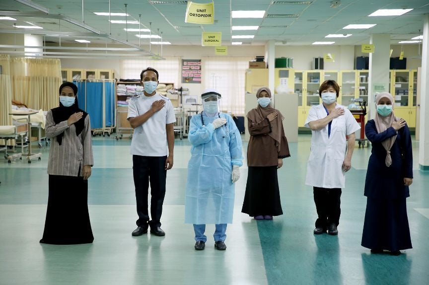 6 Healthcare Professionals Standing To Attention With Their Arms Across Their Chests, As If Reciting A Pledge, In A Malaysian Hospital