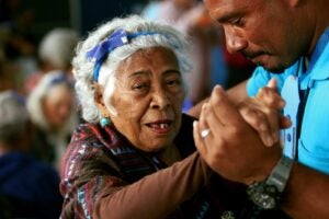 an elderly woman being supported and her hand held by a young man who looks like her son