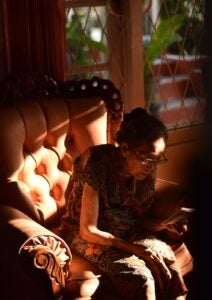 Old Lady Sitting In An Armchair Reading A Book During Dusk Or Dawn