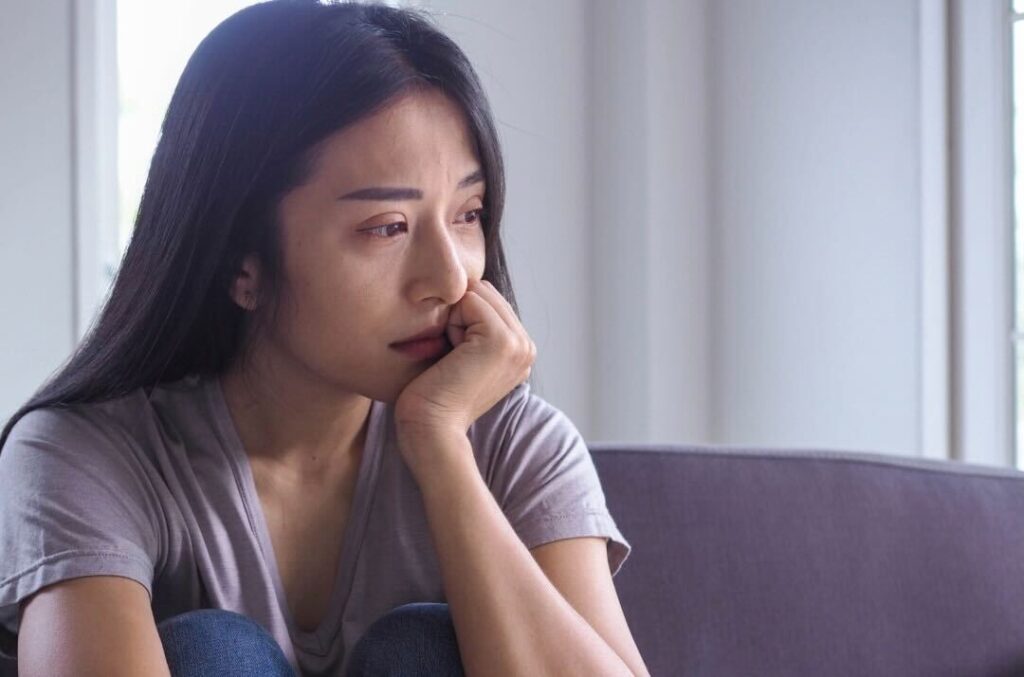 A Woman Crying And Looking Into The Distance While Sitting On A Couch In The Living Room In Broad Daylight