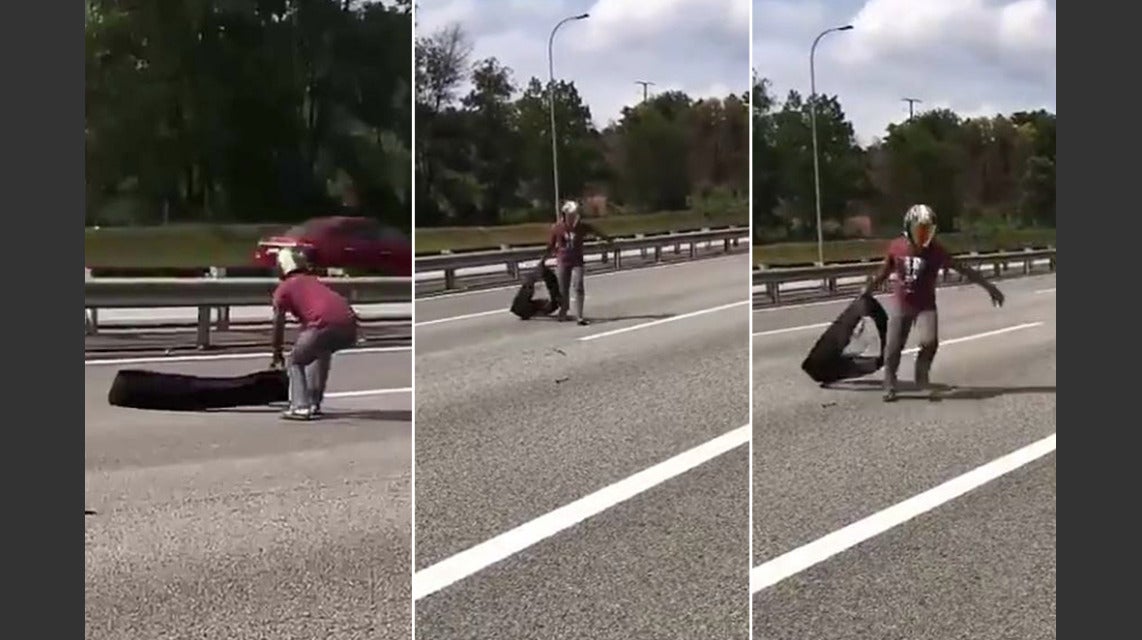 A man removes a tire from the highway at risk to his own life, image via Rojak Daily.