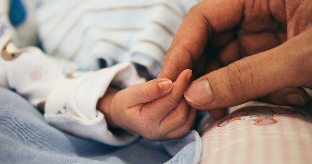 An Adult Hand Gently Holding A Baby'S Hand