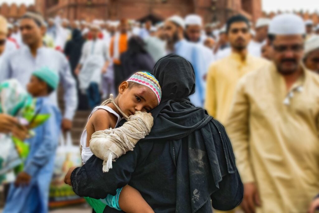 A Muslim Woman Holding A Young Boy While Walking Through A Crowd. Image Via Unsplash.
