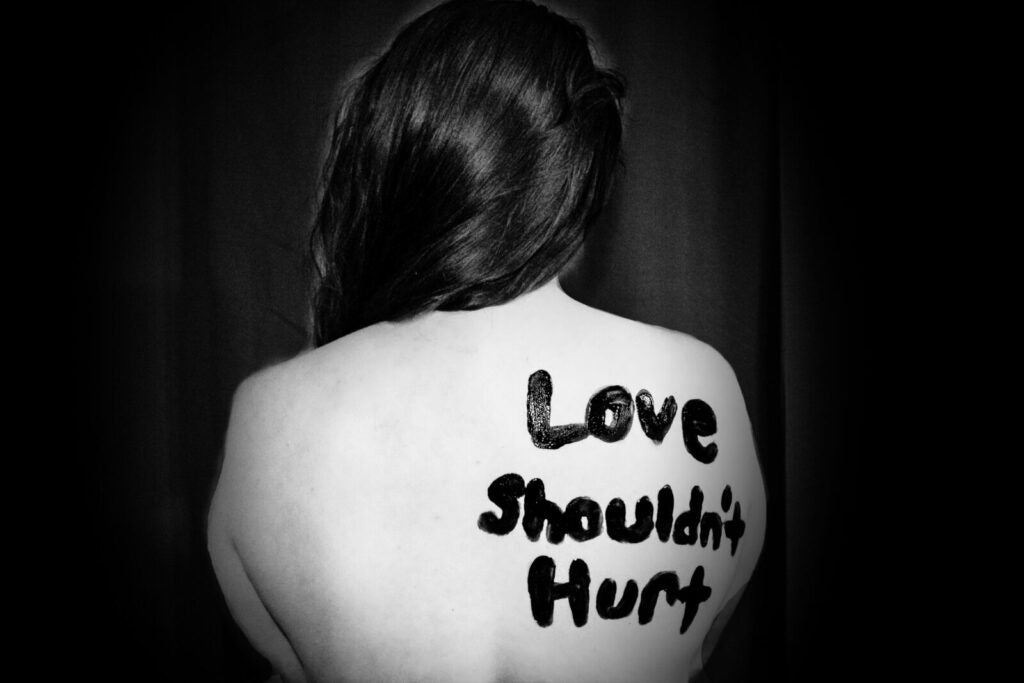A Person Whose Back Has Been Painted With The Words: Love Shouldn'T Hurt. Image Via Unsplash.
