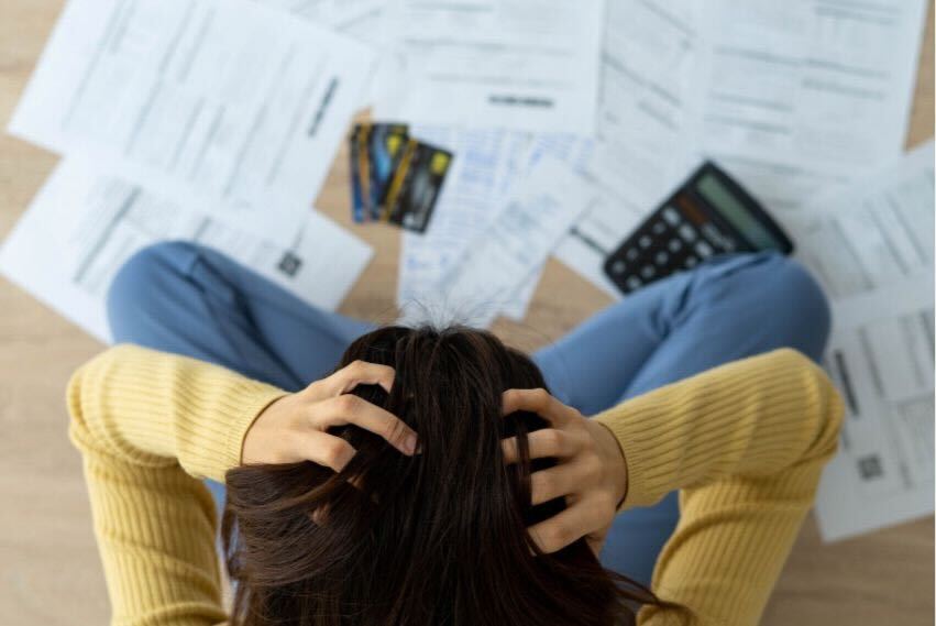 Woman Holding Her Head In Panic As She Looks At All Her Bills And Statements On The Floor In Front Of Her
